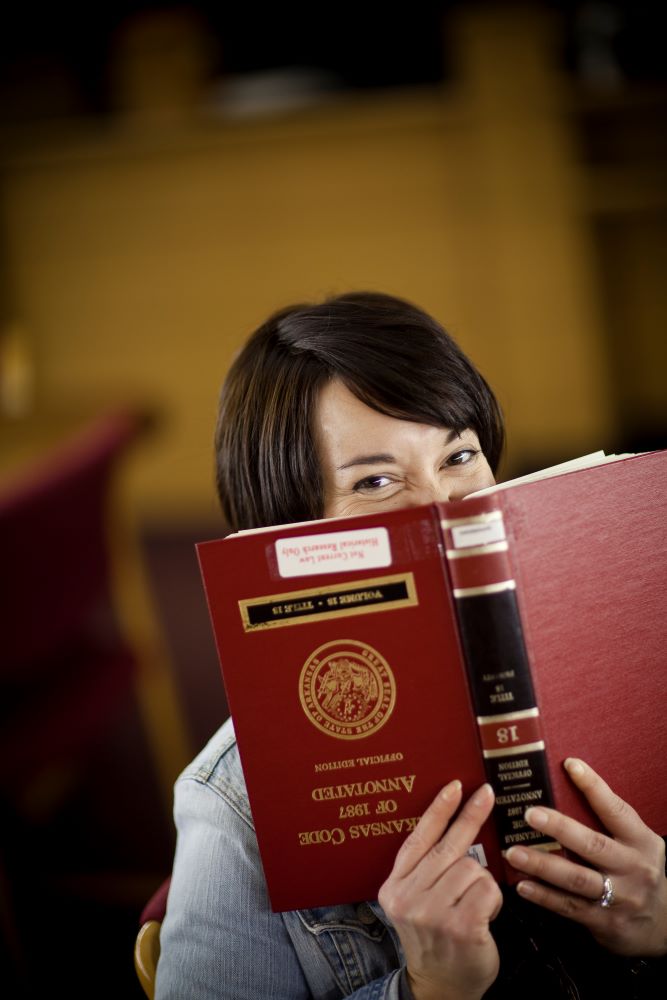 Tonya Oaks Smith having fun on a photo shoot at UA Law, holding law book upside down with smiling eyes looking over. 