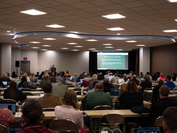 patrick kelly presenting to a full room; rows of tables