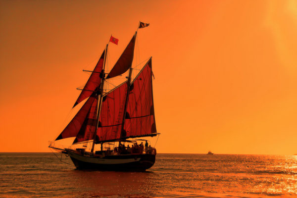 pirate ship at sea and sunset - glow of orange sky - pirate skull and crossbones flags