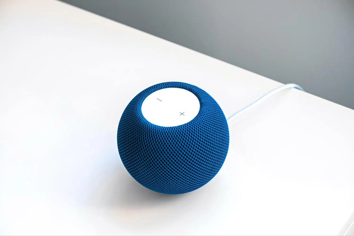 A blue smart speaker sits on a white desk.