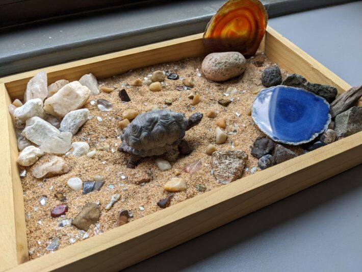 A small wooden sandbox with a turtle figurine and pebbles