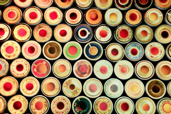 A top-down view of different teacups, all different colors and designs, filled with tea that is also different colors and design
