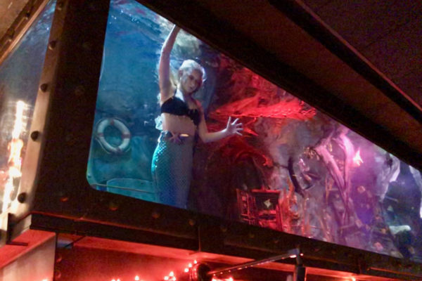 a mermaid performs in an aquarium atop a bar