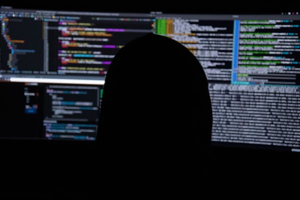 A person in shadow looks at a glowing computer screen in a dark room